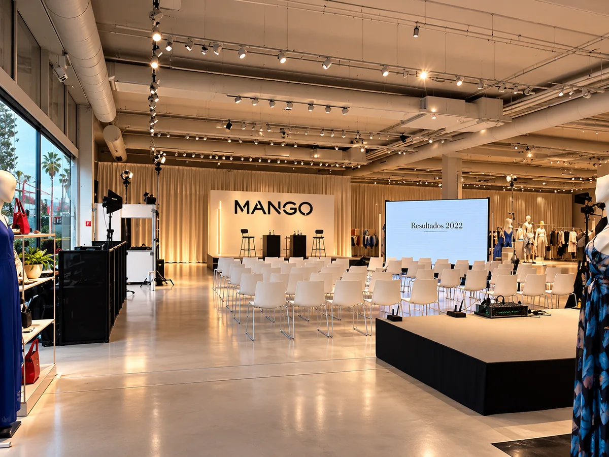 Presentación en tienda de Mango, con sillas blancas, escenario con el logo y pantalla de presentación.